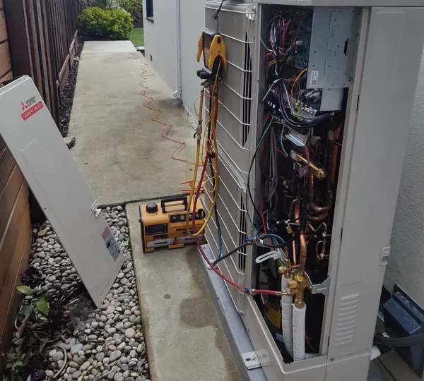 A heat pump outdoor unit with its service panel off beside a San Mateo home