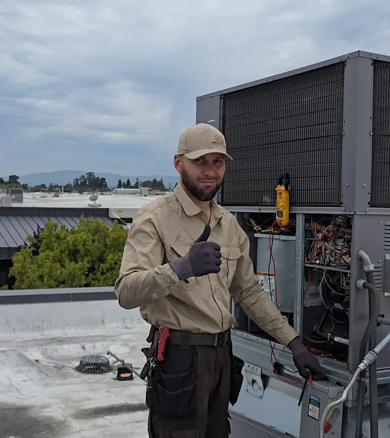 A technician gives a thumbs up beside an open rooftop unit.