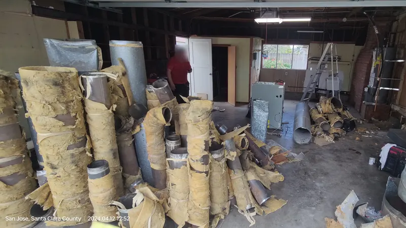 A garage floor crowded with old round metal ducts wrapped in yellowed, peeling insulation