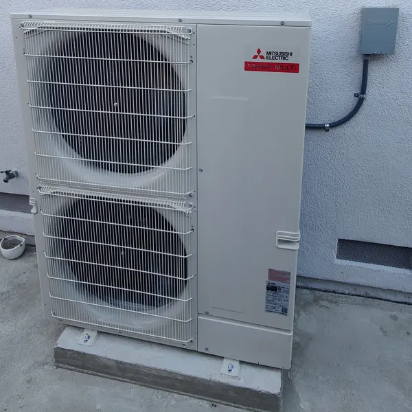 A new Mitsubishi Electric outdoor unit on a concrete pad beside a house
