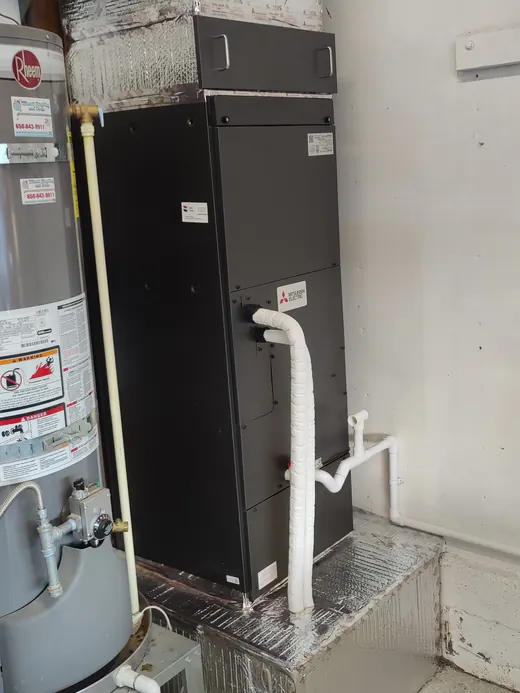 A new black air handler on a drip platform beside a water heater in a garage