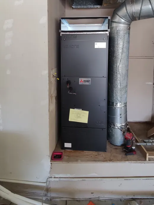 A black air handler in a closet with silver flex duct
