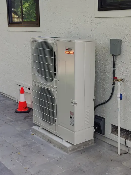 A Mitsubishi Electric Smart Multi outdoor unit on a concrete pad along a stucco wall