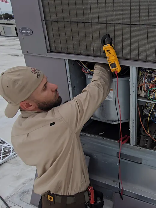 A technician clamps a meter on a wire inside an open Carrier rooftop unit